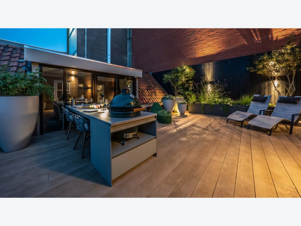 COOXS Create, Maatwerk buitenkeuken met Big Green Egg en aangebouwde buitentafel op een dakterras in Zevenbergen bij avondlicht