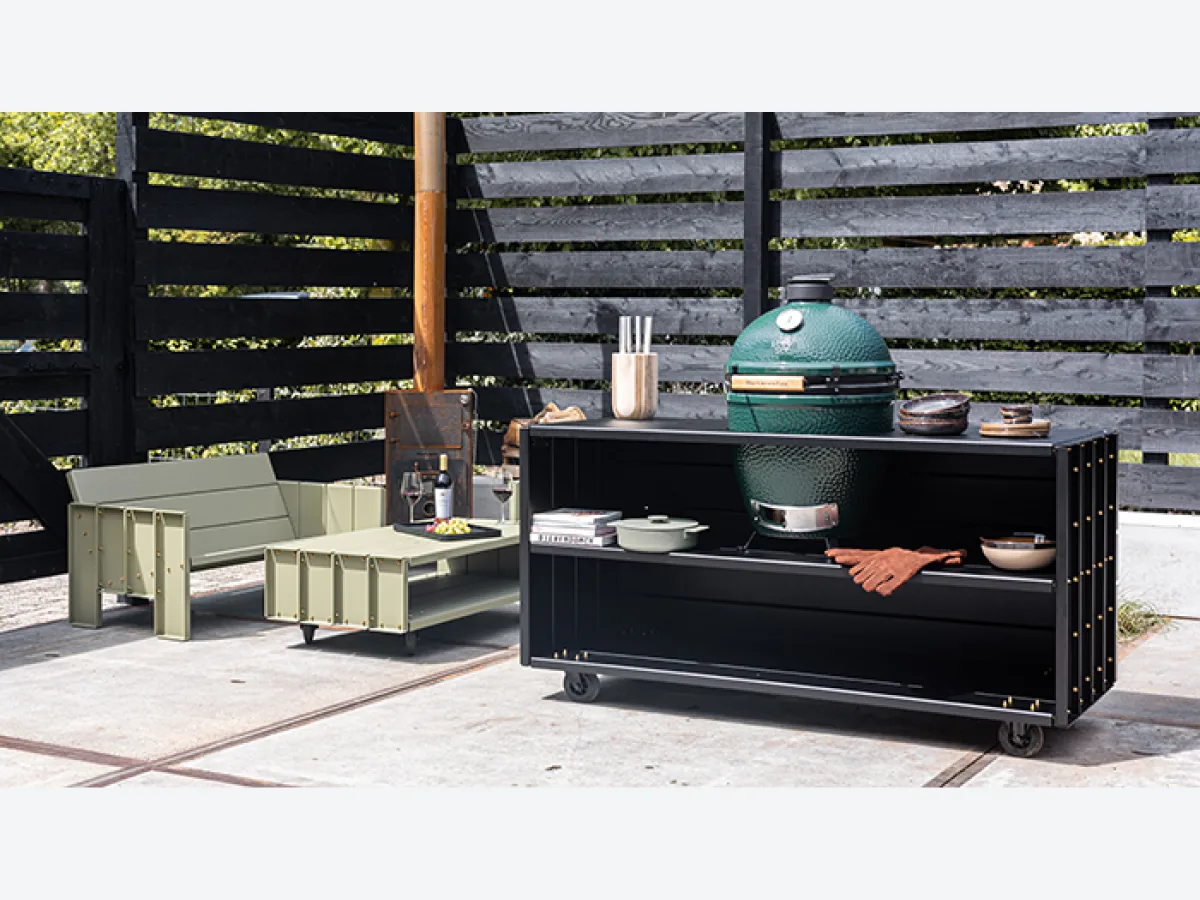 DWARS Kamado Table, Kamado Table met Big Green Egg op een terras voor een zwarte schutting, met een loungeset uit dezelfde collectie links; klein bestand van 700 pixels breed