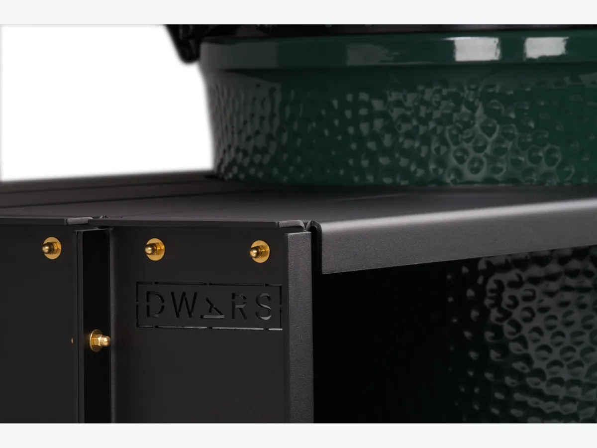DWARS Kamado Table, Detail van het aluminium blad met uitgesneden DWARS-logo, messing bouten en de onderkant van een Big Green Egg