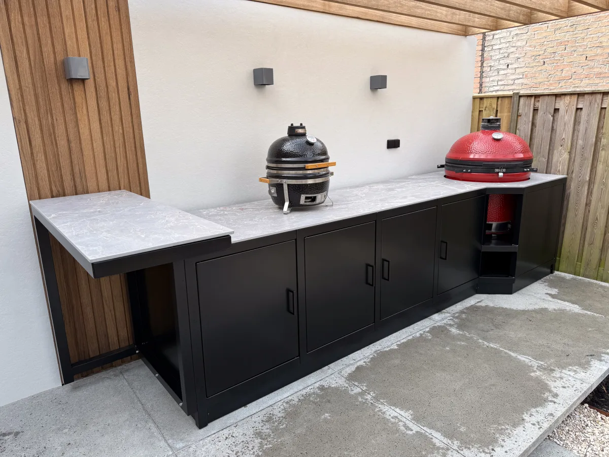 Fieldsman Modulaire buitenkeuken, Lange zwarte modulaire buitenkeuken met Fior di Bosco werkblad en twee kamados onder een overkapping (portfolio Alkmaar)