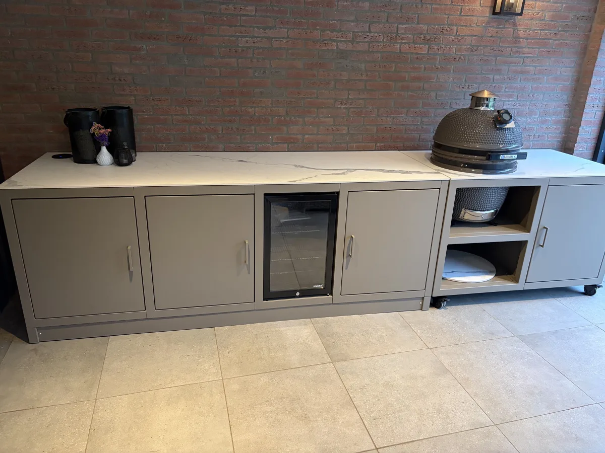 Fieldsman Modulaire buitenkeuken, Beigegrijze modulaire buitenkeuken met Statutario werkblad, koelkast en kamado tegen een bakstenen muur (portfolio Den Bosch)