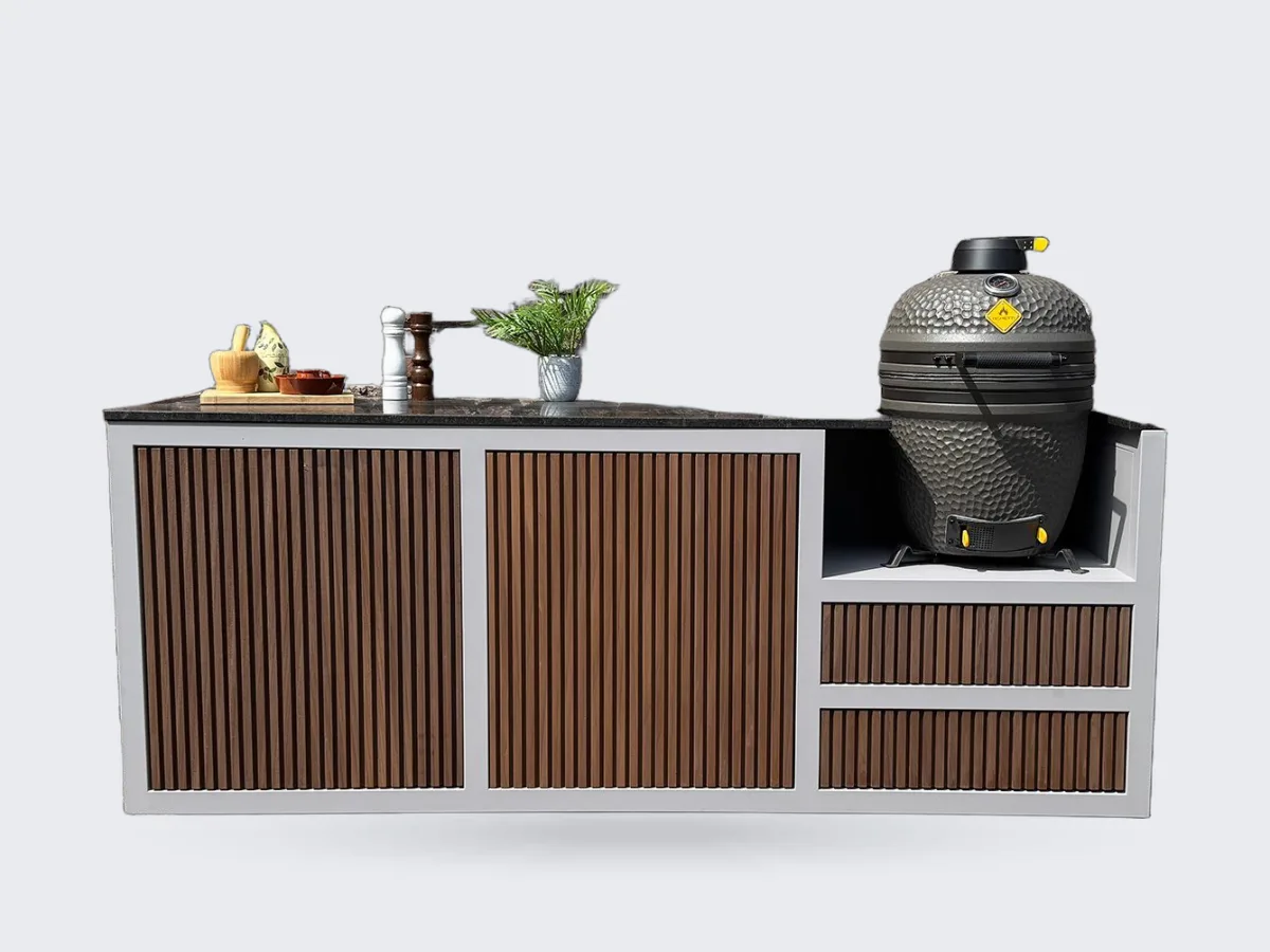 HoutenmeubelsXL Bandung, Buitenkeuken Bandung van thermohout met grijs stalen frame en natuurstenen blad, met kamado rechts, recht van voren voor een bakstenen muur