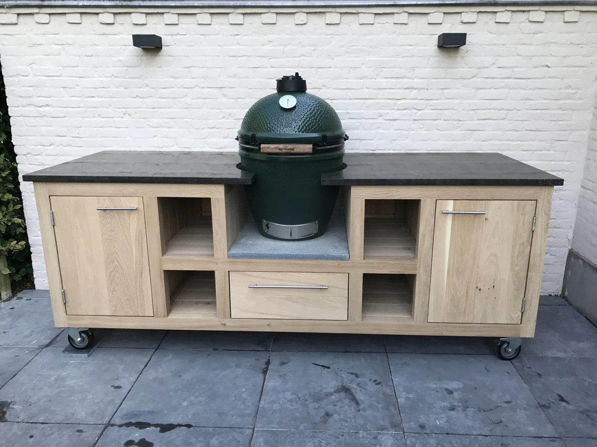 Kamado Buitenkeuken Maatwerk buitenkeuken, Verrijdbare eiken buitenkeuken met donker natuurstenen werkblad, Big Green Egg in het midden, open vakken, lade en deuren voor een witte muur
