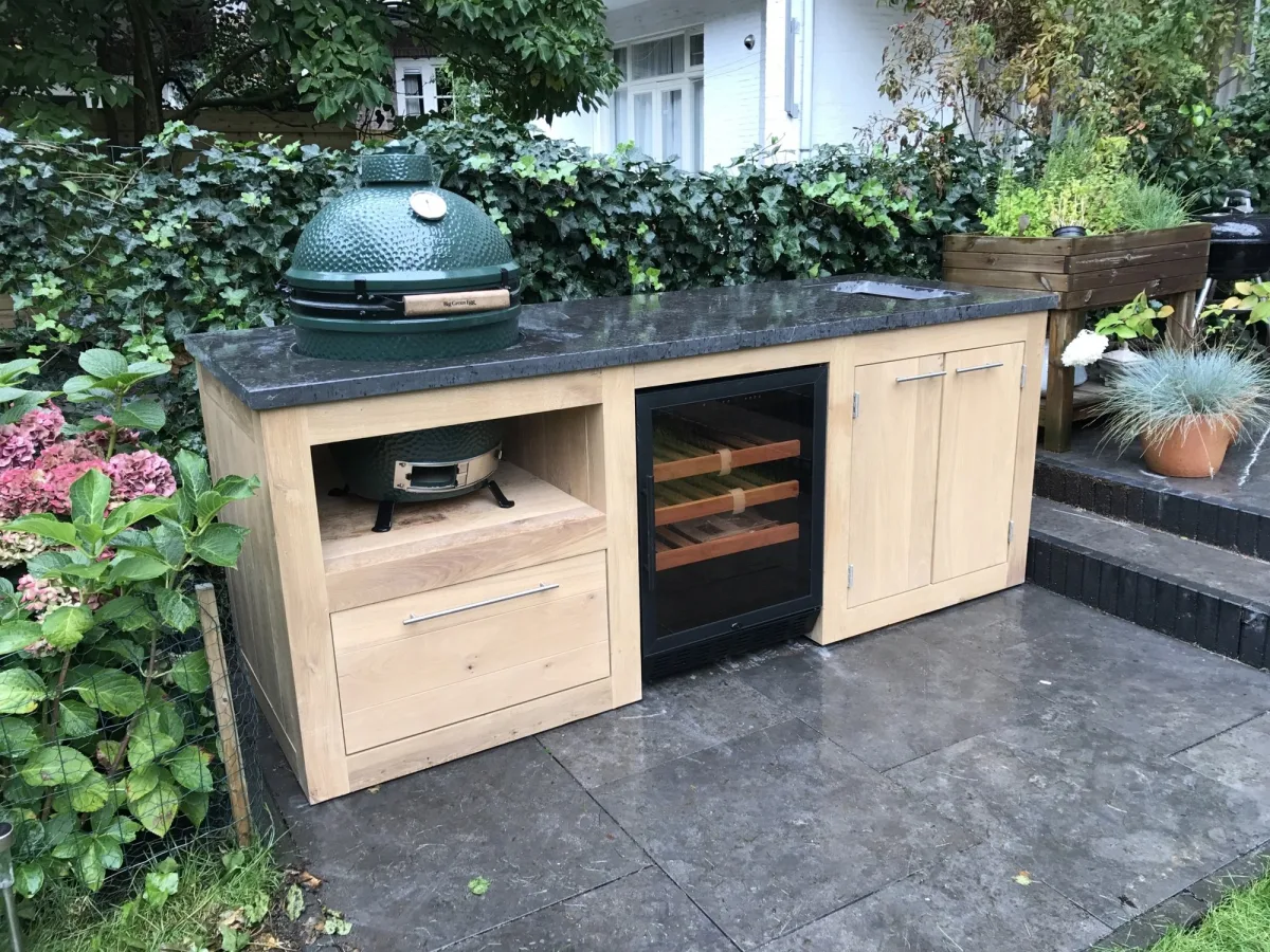 Kamado Buitenkeuken Maatwerk buitenkeuken, Eiken buitenkeuken met Big Green Egg, inbouwkoelkast en natuurstenen werkblad tussen hortensia's in een tuin