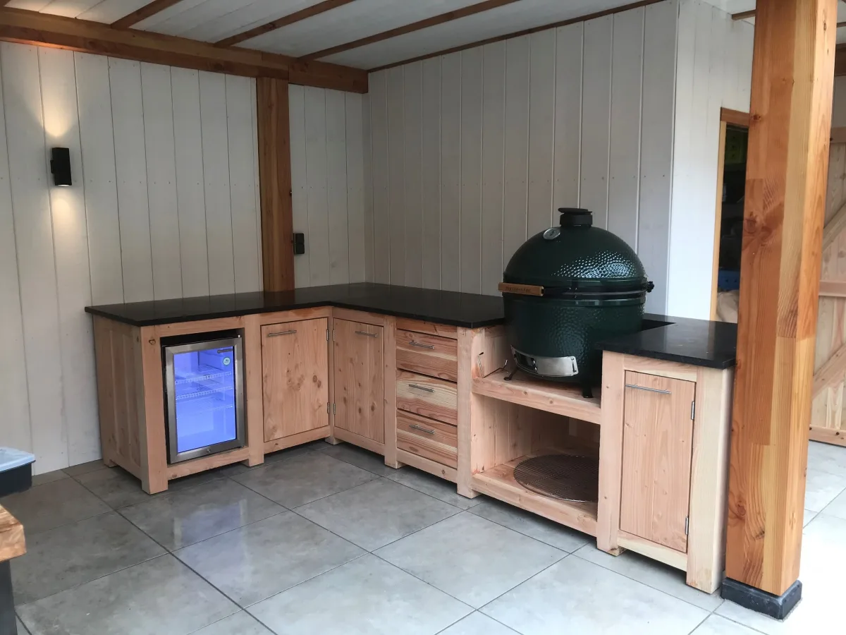Kamado Buitenkeuken Maatwerk buitenkeuken, Hoekopstelling van douglas met Big Green Egg, koelkast, laden en natuurstenen werkblad onder een witte overkapping