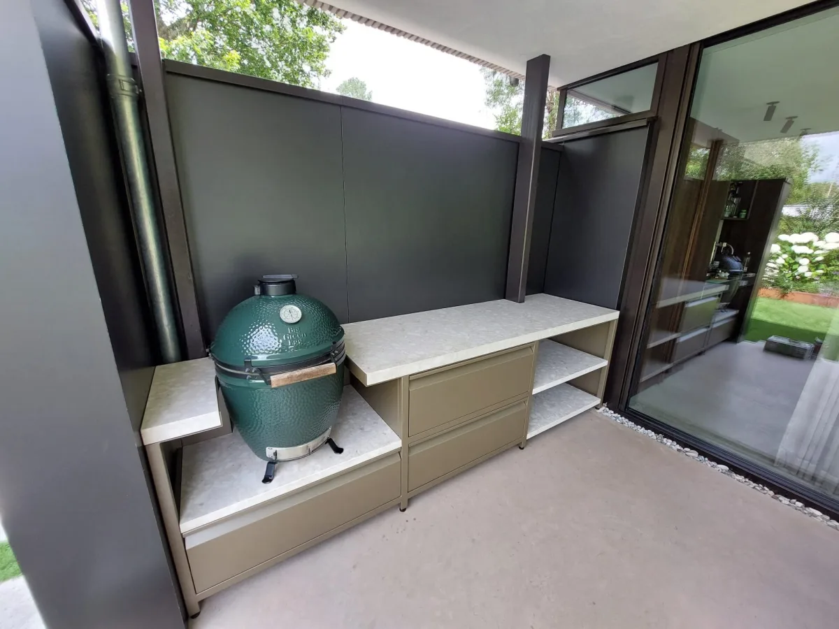 Robuust Maatwerk Vaste buitenkeuken, Vaste buitenkeuken van bronskleurig gecoat staal met keramisch blad en Big Green Egg Large links, driekwart van linksvoor in een overdekte buitenruimte
