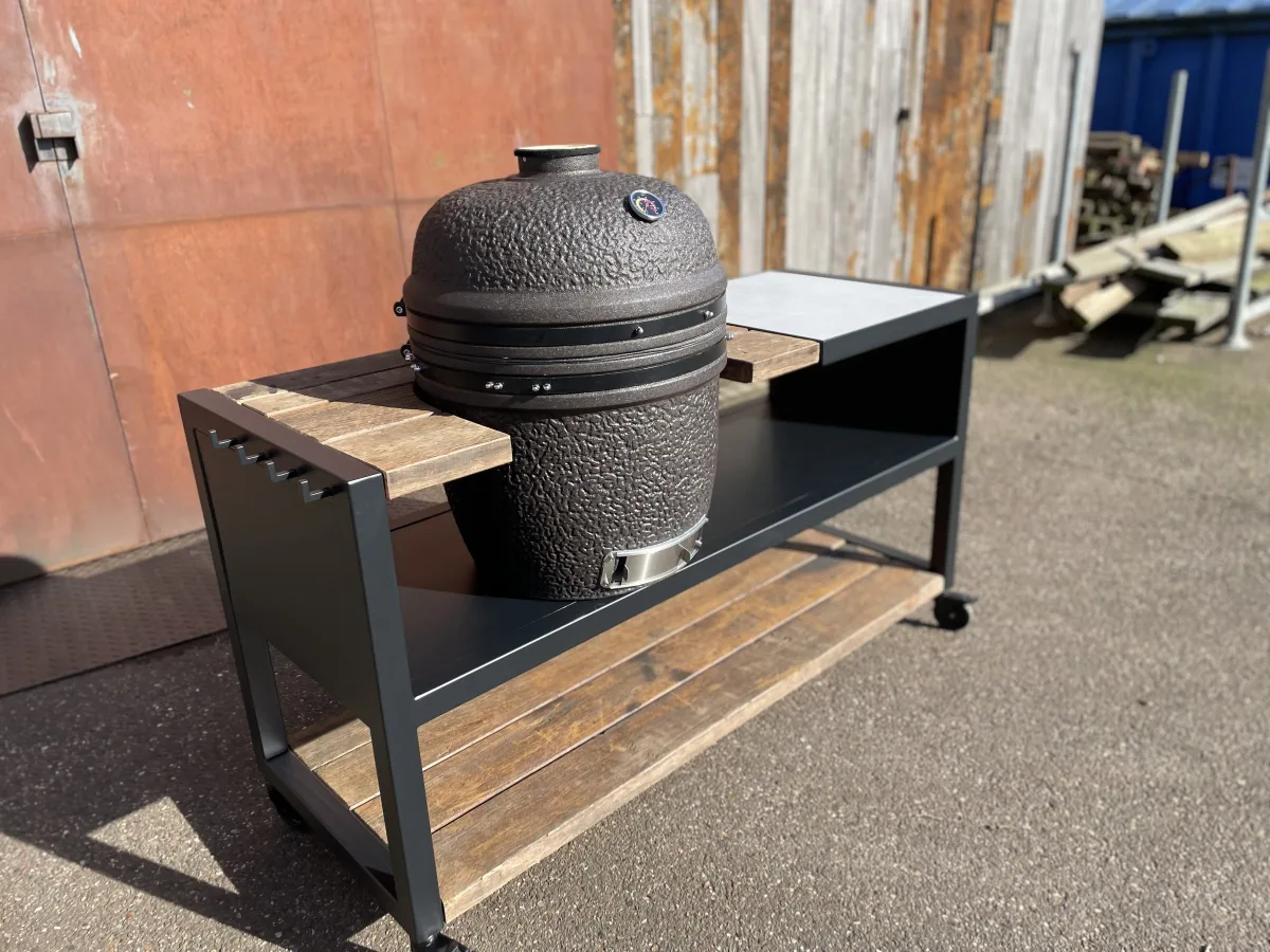 Robuust Maatwerk Verrijdbare buitenkeuken, Verrijdbare buitenkeuken van zwart staal met azobe blad, betonnen blad en kamado in de uitsparing, driekwart van linksvoor met de haakjes aan de zijkant