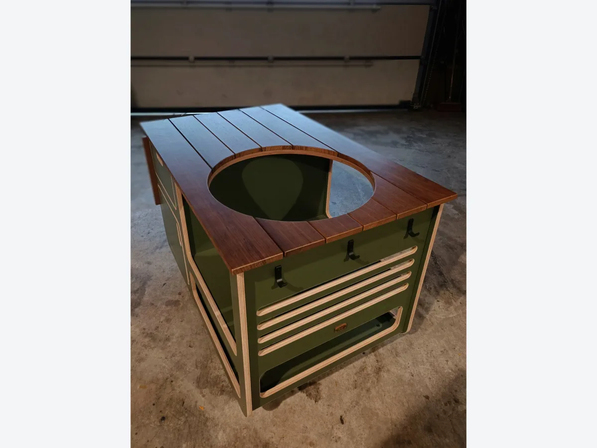 Studio RUUB Buitenkeuken staal en hout, Detail van het frake werkblad met ronde sparing voor de kamado en de olijfgroene kast met lamellen, in de werkplaats