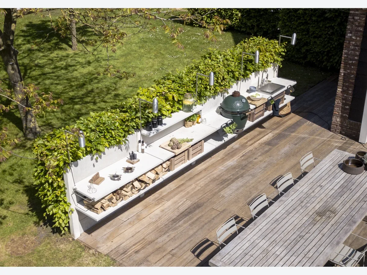 WWOO Beton, WWOO betonnen buitenkeuken in wit met Big Green Egg en spoelbak, van bovenaf gezien langs een haag op een houten terras